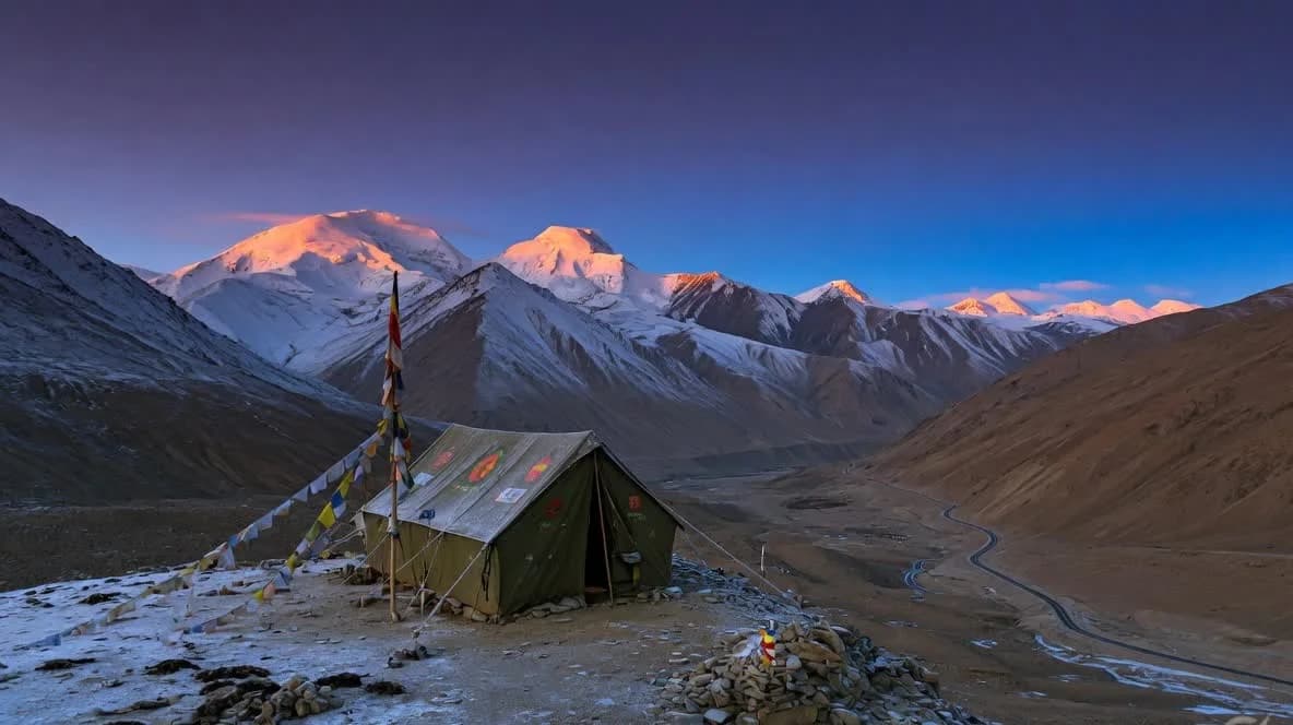 A canvas tent at blue hour in Ladakh with snow peaks and a valley road below
